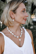 Fiora baroque pearl necklace with gemstone tassel and gold toggle clasp, worn with a white dress